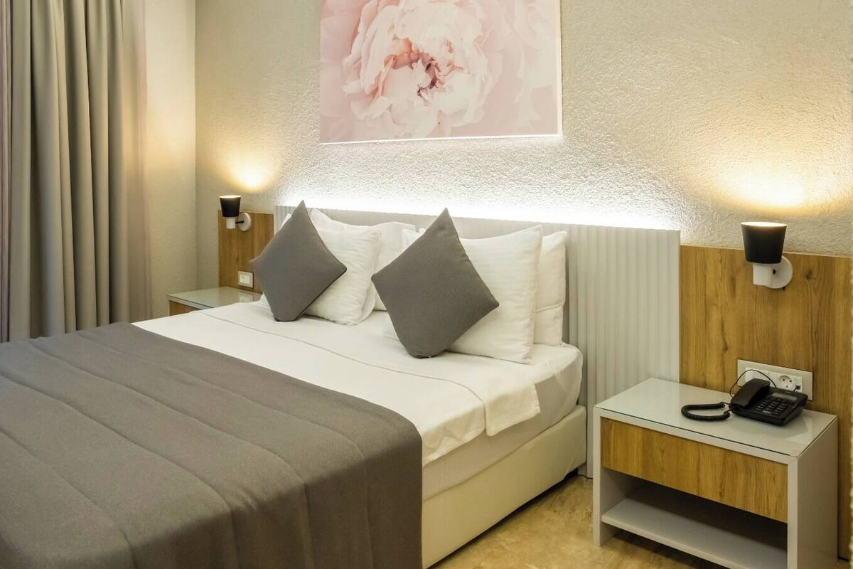 A hotel room with a bed, two bedside tables, a phone, and a painting on the wall.