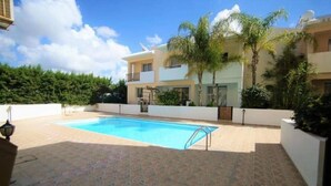 A swimming pool with a tiled deck, surrounded by a white wall and palm trees. - Beautiful Apartment With Pool in Paphos, Cyprus (Paphos)