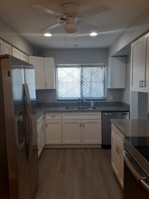 A modern kitchen with white cabinets, a stainless steel refrigerator, a dishwasher, and a granite countertop. - Cozy beach home within walking distance to the beach (Satellite Beach)