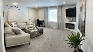 Un salon avec un canapé beige, une table basse, une cheminée, un téléviseur et une fenêtre avec des rideaux.