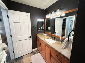A bathroom with a white door, a sink with a mirror above it, and a towel hanging on the wall.