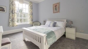 A bedroom with a single bed, a nightstand, a chair, and a window with floral curtains. - 98 Fountain Villas - sleeps 16 guests  in 7 bedrooms (Matlock Bath)