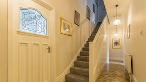 A hallway with a staircase, a door with a stained glass window, and framed pictures on the walls. - 98 Fountain Villas - sleeps 16 guests  in 7 bedrooms (Matlock Bath)