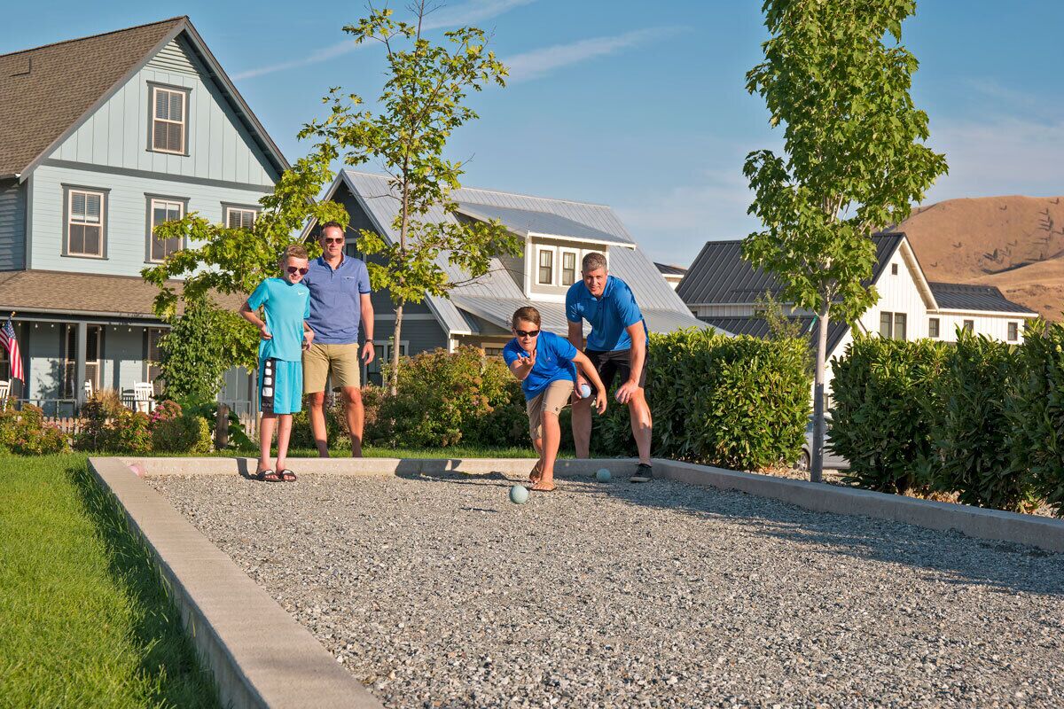A residential area with houses, a gravel driveway, and a person playing croquet.
