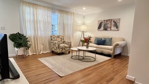 Un salon avec un plancher en bois, un canapé, un fauteuil, une table basse, une lampe et un téléviseur.