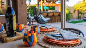 A table set with a bottle of wine, colorful cups, and a woven placemat. - Polynesian Villa w/Private Pool & Tiki Bar Oasis (Indio)