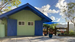 A building with a green exterior and blue roof, featuring two windows and a blue awning. - Island Escape for Two, Class and Comfort (Coral Bay Quarter)