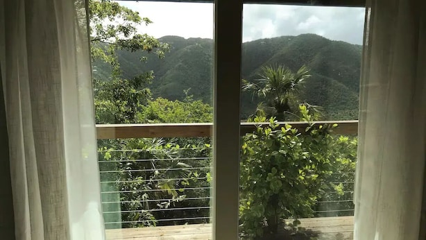 A view through a window with a wooden deck and greenery, overlooking a mountainous landscape. - Island Escape for Two, Class and Comfort (Coral Bay Quarter)