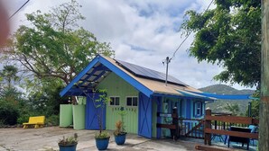A small, colorful building with a blue roof and green walls, surrounded by potted plants and a wooden fence. - Island Escape for Two, Class and Comfort (Coral Bay Quarter)