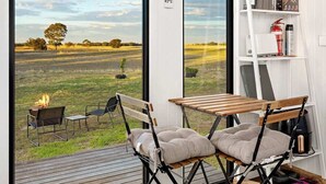 A modern room with large windows, a wooden deck, a table with chairs, and a shelf with various items. - Avondale Heights by Tiny Away (Banyena)