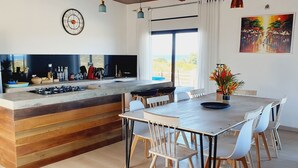 Et moderne køkken med en træø, et spisebord med stole, et stort vindue med gardiner og et billede på væggen.