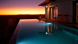 En moderne uendelig pool med krystalklart vue over solnedgangen, et barområde med barstole og en stor skydedør af glas.