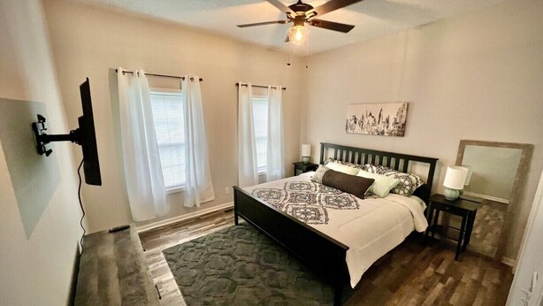 A bedroom with a bed, a ceiling fan, a nightstand, a lamp, and a window with curtains. - 2 br home close to downtown and Lucas Oil. Pet Friendly! (Indianapolis)