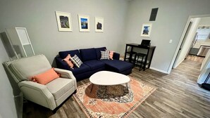 A living room with a sofa, armchair, coffee table, and a rug. There are framed pictures on the wall and a small table with a laptop. - 2 br home close to downtown and Lucas Oil. Pet Friendly! (Indianapolis)