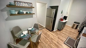 A modern kitchen with a stainless steel refrigerator, a coffee machine, and a microwave. There is a dining table with four chairs and a 'WELCOME' sign above it. - 2 br home close to downtown and Lucas Oil. Pet Friendly! (Indianapolis)