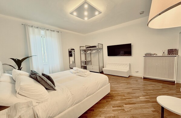 A modern bedroom with a large bed, a wardrobe, a TV, and a bedside table.