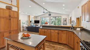 A spacious kitchen with wooden cabinets, a large island, and a dining table. - Riverfront 4 bed/3bath home on Bitterroot River plus a Pickleball Court  (Hamilton)