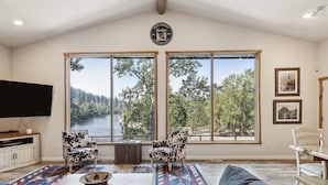 A spacious living room with large windows, a flat-screen TV, and a cozy seating area. - Riverfront 4 bed/3bath home on Bitterroot River plus a Pickleball Court  (Hamilton)