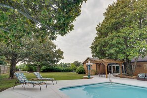 Relax by the pool surrounded by lush greenery and a pergola providing shade.