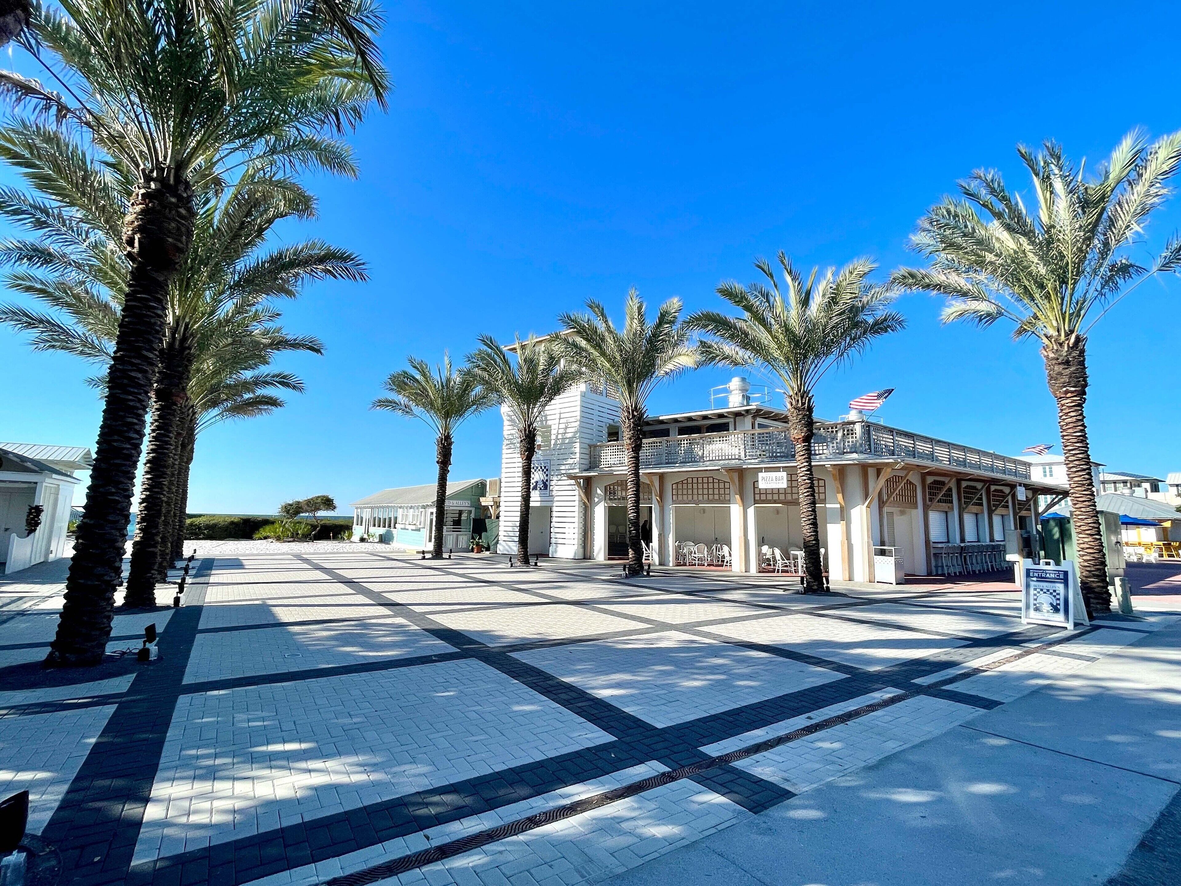 A building with a pizza shop, palm trees, and a clear blue sky.