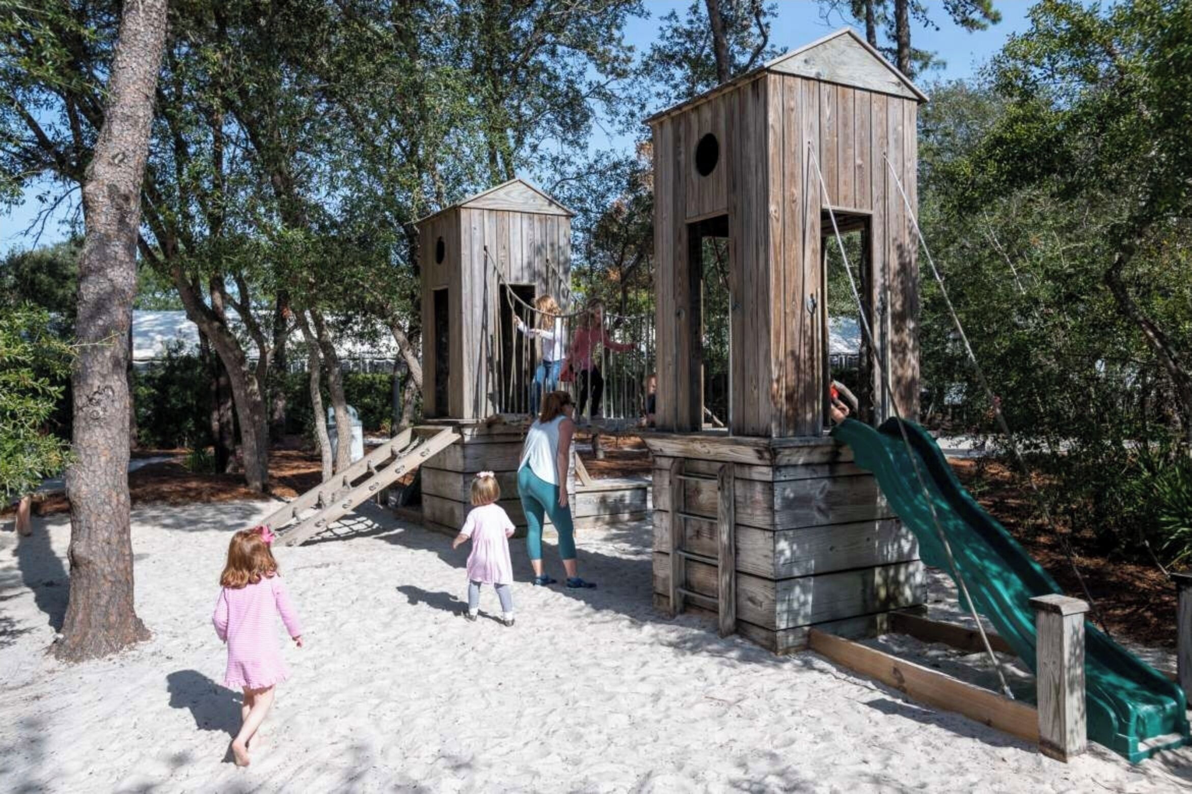 Une structure de jeu en bois, dotée d’un toboggan et d’éléments d’escalade, entourée d’arbres.