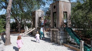 Une structure de jeu en bois, dotée d’un toboggan et d’éléments d’escalade, entourée d’arbres.