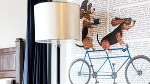 Olohuone, jossa on harmaa sohva, sininen tuoli, lattiavalaisin ja seinälle kiinnitetty pyöräaiheinen taideteos.