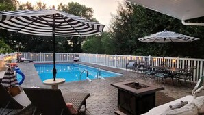 An outdoor pool area with lounge chairs, umbrellas, and a fire pit.