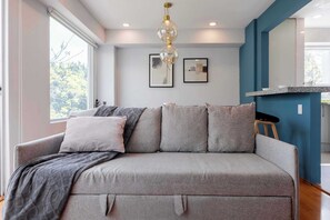 A modern living room with a grey sofa, a hanging light fixture, and framed artwork on the wall.