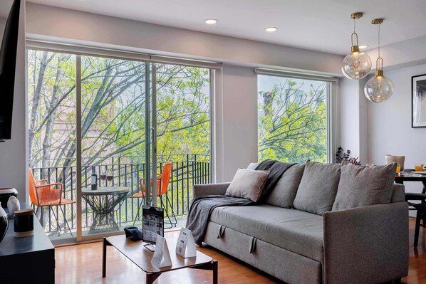 A modern living room with a sofa, a coffee table, and a balcony with chairs.