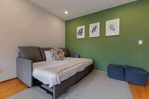 A bedroom with a bed, grey sofa, and a green wall with leaf art.
