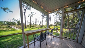 A covered patio with a wooden table and chairs, overlooking a grassy area with trees and a wooden bridge. - Ground Level, Bayside Retreat w/ bay access! Dogs OK, Large Pond (Eastpoint)