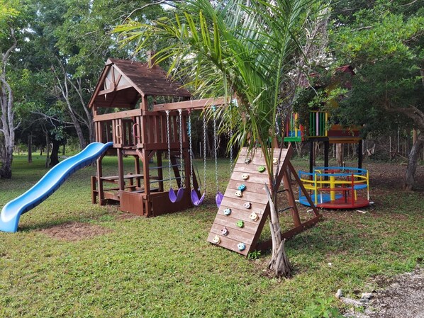 A wooden play structure with a slide and climbing wall, surrounded by trees. - Enjoy a natural environment at Paradise Ranch (La Cotita)