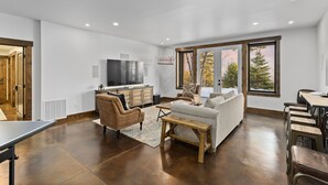 A spacious living area with a large flat-screen TV, a sofa, a coffee table, and a dining table with chairs.