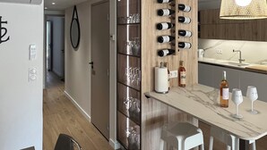 A modern kitchen with a wooden cabinet, wine bottles, and glasses on the wall, a marble countertop, and a hanging light fixture.