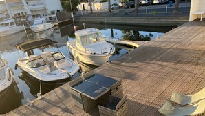 A wooden deck with a small table and a chair, overlooking a marina with several boats docked.
