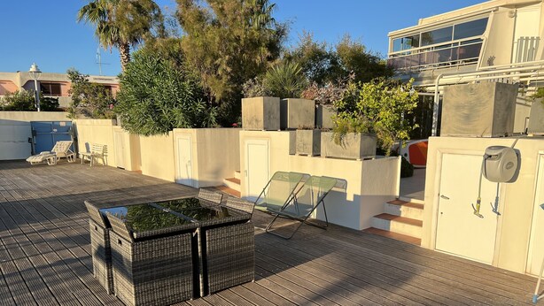 A rooftop terrace with a wooden deck, lounge chairs, and a small garden area with potted plants.