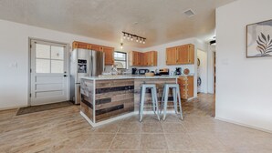 A modern kitchen with a central island, wooden cabinets, and a stainless steel refrigerator.