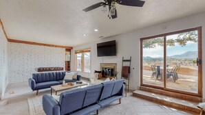 A spacious living room with a large window, a fireplace, and a ceiling fan.