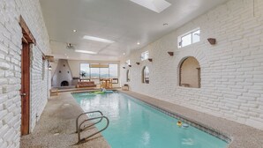 An indoor swimming pool with white brick walls, a wooden door, and a view of the mountains through a large window.