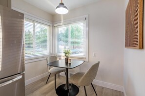 Une cuisine moderne avec un réfrigérateur en acier inoxydable, une table noire avec deux chaises et une plante en pot posée sur le rebord de la fenêtre.