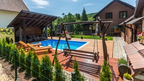 A backyard with a wooden deck, a swing set, a swimming pool, and a fenced area with potted plants. - Holiday House Papuk is Located in Park of Nature (Brestovac)