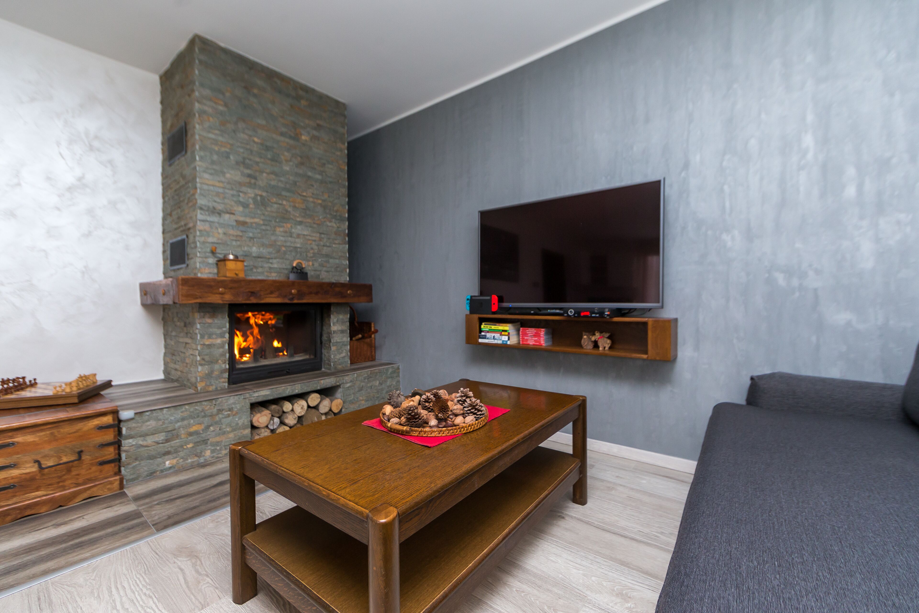 A living room with a stone fireplace, a wooden coffee table, a grey sofa, and a mounted TV.