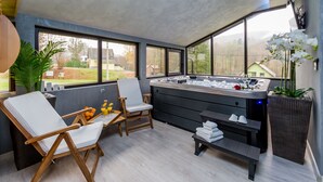 A modern spa room with a hot tub, two lounge chairs, a bench, and a large window offering a view of the outdoors. - Holiday House Papuk is Located in Park of Nature (Brestovac)