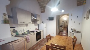 Cocina compacta con comedor, que incluye una mesa y sillas de madera, horno empotrado y un refrigerador pequeño.