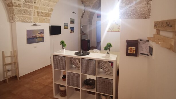 Una habitación rústica con techo de ladrillo, una consola blanca con objetos decorativos y una escalera de madera apoyada en la pared.