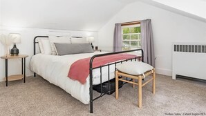 A bedroom with a bed, a nightstand, a lamp, a window with curtains, and a radiator. - Charming 3 bedroom, 2 bathroom Catskills cottage (Saugerties)