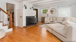 A spacious living room with a fireplace, a large white sofa, and a wooden staircase. - Charming 3 bedroom, 2 bathroom Catskills cottage (Saugerties)