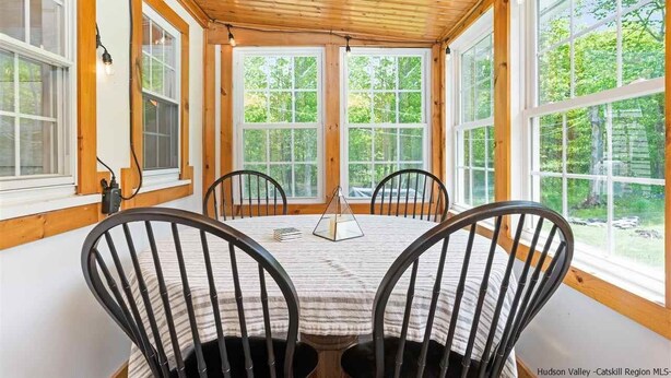 A cozy room with a wooden ceiling, large windows, and a round table with chairs. - Charming 3 bedroom, 2 bathroom Catskills cottage (Saugerties)