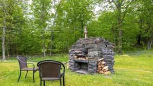 A stone-built outdoor fireplace with a chimney, surrounded by a grassy area with two wicker chairs. - Charming 3 bedroom, 2 bathroom Catskills cottage (Saugerties)